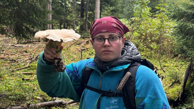 A photography of queer ecologist, Abi Young, holding a large fungus in their hand, looking to camera.